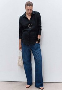 Black button-up shirt, blue wide-leg jeans, clear mesh bag, gold circular necklace, black bangles, and tan sandals. Smooth fabric and casual fit.