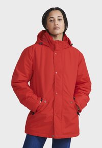 Rote isolierte Jacke mit Kapuze, mit einem Frontreißverschluss und Druckknöpfen sowie seitlichen Taschen. Glatte Textur und leicht oversized Passform.