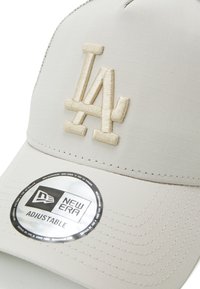 Beige adjustable cap featuring an embroidered "LA" logo and textured surface, with a circular New Era sticker on the brim.