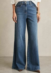 Jeans a vita alta e gamba larga realizzati in denim blu scuro. Caratteristiche includono tasche frontali, cuciture leggere e una leggera lucentezza.