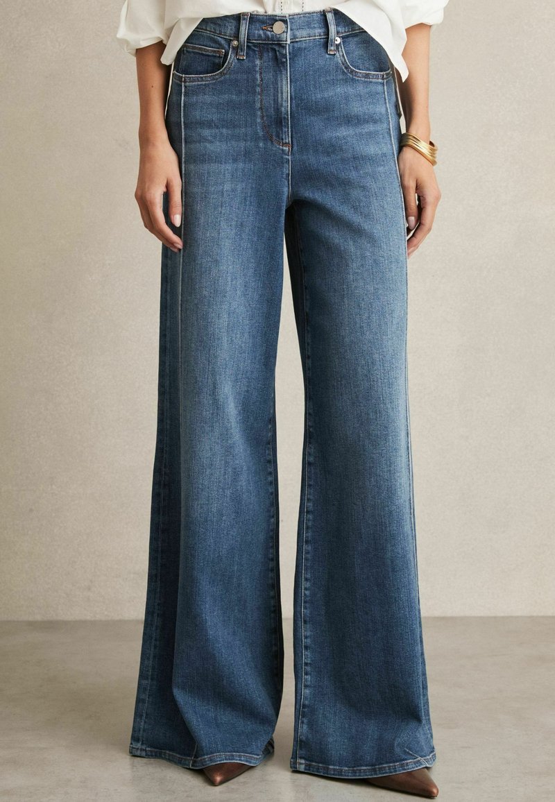 Jeans a vita alta e gamba larga realizzati in denim blu scuro. Caratteristiche includono tasche frontali, cuciture leggere e una leggera lucentezza.