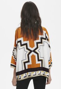 Top in stile kimono in arancione, bianco e nero con motivi geometrici. Presenta una vestibilità ampia, maniche corte e bordo dorato all'orlo.