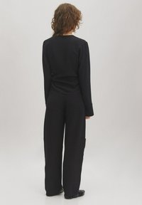 Schwarzes Langarmoberteil mit tailliertem Schnitt und lockeren Hosen mit seitlichen Taschen und einer locker Fallenden Silhouette. Texturierter Stoff.