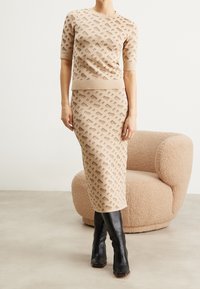 Set di maglieria a due pezzi beige con un motivo geometrico testurizzato; top a maniche corte abbinato a una gonna a tubino midi; indossato con stivali neri fino al ginocchio.