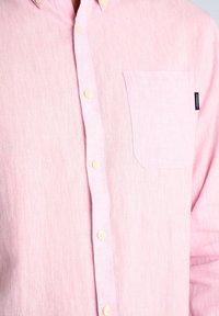 Lichtroze shirt van een gestructureerde stof, met een button-down kraag, gele knopen en een borstzak aan de linkerkant.