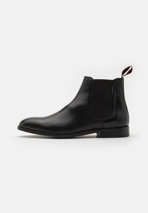 Czarne skórzane buty typu Chelsea z elastyczną boczną wstawką i pętelką do ściągania, niskim obcasem i gładkim, zaokrąglonym noskiem, widoczne od strony zewnętrznej.
