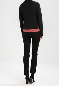 Czarna strukturalna marynarka o dopasowanym kroju, w połączeniu z różową bluzką i czarnymi dżinsami Skinny. Czarne botki na obcasie do kostki dopełniają cały look.