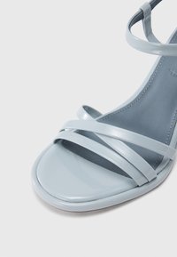 Ανοιχτό μπλε σανδάλι με γυαλιστερό, λουράκι σχεδιασμό, επίπεδη σόλα και ομαλή υφή· ελάχιστο ράψιμο κατά μήκος των άκρων.