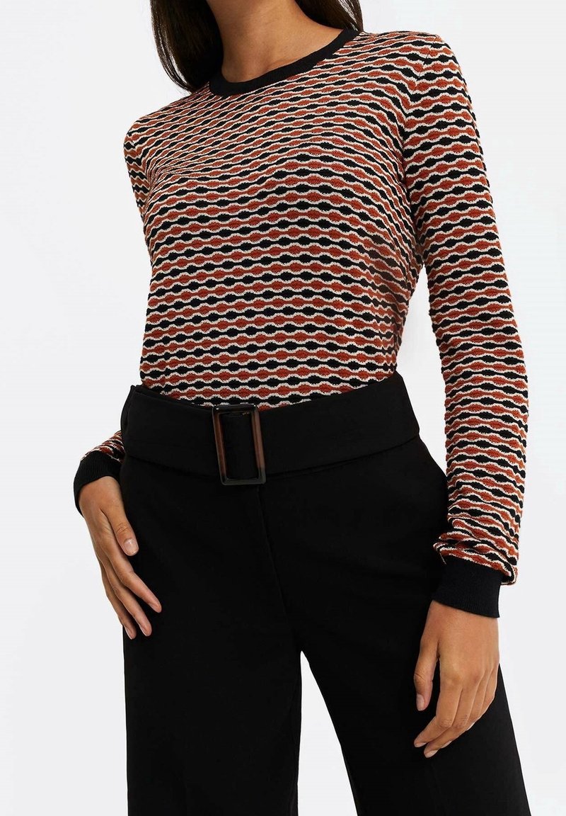 Neulottu pitkähihainen paita, jossa on aaltoileva kuvio oranssin, mustan ja kermaan sävyissä, mustat resorireunukset kaula-aukossa ja hihansuissa. Yhdistetty mustiin housuihin.