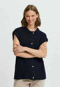 Marineblauer gestrickter ärmelloser Pullover mit kurzem Ärmel, geripptem Halsauschnitt und vertikaler Knopfleiste mit großen goldenen Knöpfen. Weiche Textur.