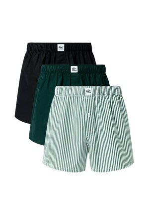 Tri páry boxeriek Lacoste v čiernej, tmavozelenej a zelenej farbe s bielymi vertikálnymi pruhmi, každé s elastickým pásom a značkovou etiketu.