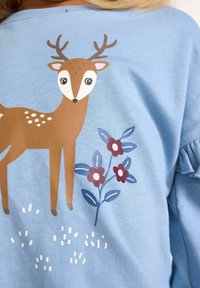 Jasnoniebieska bluza z ilustracją jelenia z rogami, brązowym ciałem, białymi plamkami i kwiatami w ciemnoniebieskim i różowym kolorze.