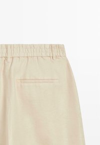 Pantalon en tissu beige avec une taille élastique, des passants pour ceinture et une unique poche arrière horizontale.
