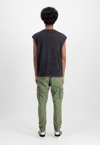 Μαύρη αμάνικη μπλούζα με απαλή υφή, σε συνδυασμό με πράσινα cargo παντελόνια που διαθέτουν πλευρικές τσέπες και ελαστικές μανσέτες.