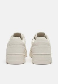 Pantofi sport bej cu partea superioară din țesătură netedă, design rotunjit, profil jos și talpă din cauciuc texturată în contrast. Prezintă detalii subtile de cusături.