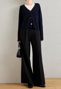 Námořnický žebrovaný kardigan s dlouhými rukávy a zapínáním na tři knoflíky, spojený s černými kalhotami s širokými nohavicemi. Jednoduchá černá kabelka.