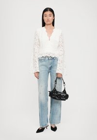 Witte kant lange mouwen top met een V-hals, gecombineerd met versleten lichtblauwe jeans en een kleine zwarte handtas met studs, en zwarte hakken.