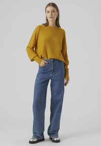 Senapsfärgad stickad tröja med texturerat diamantmönster, kombinerad med högmidjade blå jeans och metalliska ankelstövlar. Enkel och avslappnad outfit.