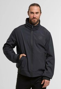Black, zip-up softshell jacket with high collar, elastic cuffs, side pockets, and a logo on the chest. Made from smooth, durable fabric.