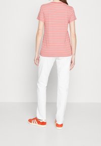Paskowana koszulka z krótkim rękawem w kolorze koralowym i białym, zestawiona z białymi spodniami i czerwonymi trampkami z białymi paskami. Gładki materiał, swobodny fason.