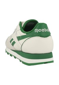 Białe sneakersy z zielonymi akcentami, wykonane z skórzanej cholewki i zamszowymi detalami. Zawierają teksturowaną podeszwę oraz logo Reebok na pięcie.