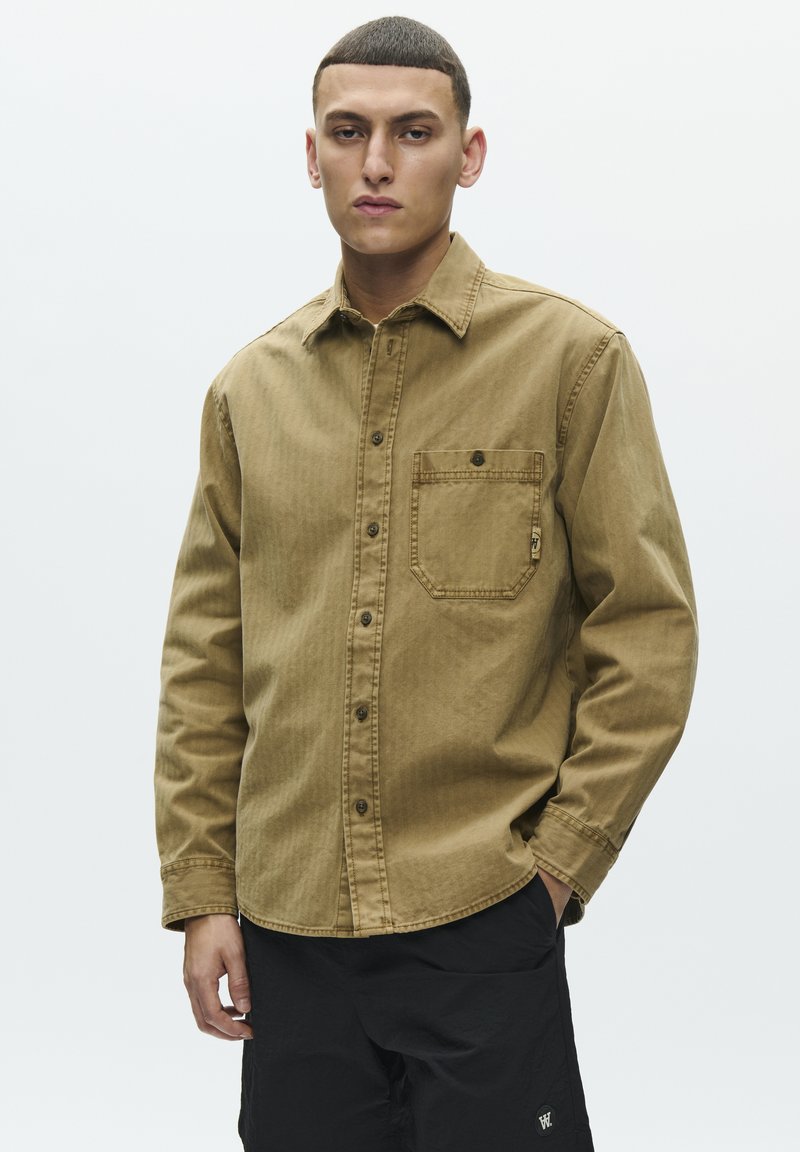 Chemise marron boutonnée avec une poche poitrine et un tissu texturé. Présente des manches longues et un col standard, conçue pour une coupe décontractée.