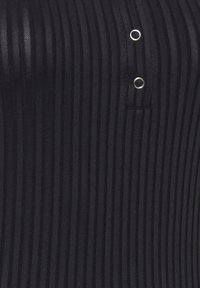 Svart ribbad topp med tunna vertikala ränder, en figurnära passform och två silverringdetaljer vid halsen. Mjuk textur.