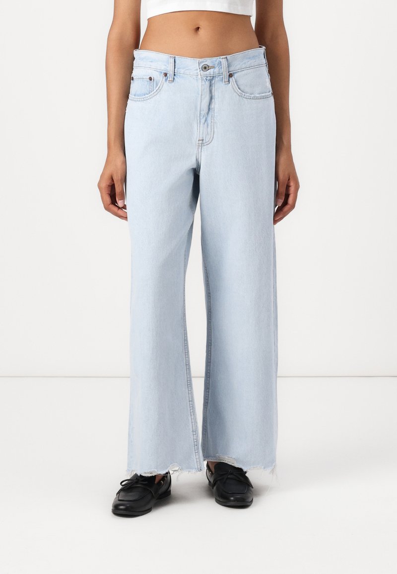 Ljusblå vida denimjeans med råkant, fem fickor och subtila sömdetaljer. Matchas med svarta skor.