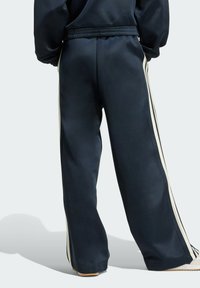 Pantalones de chándal azul marino con un ajuste relajado, que presentan rayas verticales en crema a los lados y una textura suave y lisa. Incluye cinturilla elástica.