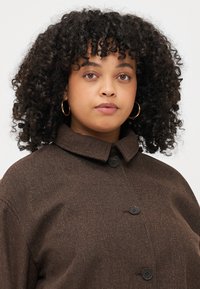 Brown textured coat with a collar, featuring large black buttons. The fabric has a subtle pattern, and the fit is relaxed.