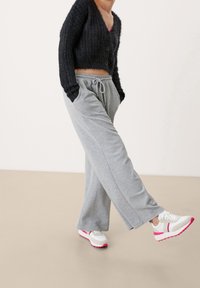 Šedé tepláky s páskem na šňůrku, kombinované s černým strukturovaným kardigánem. Bílé tenisky s růžovými akcenty.