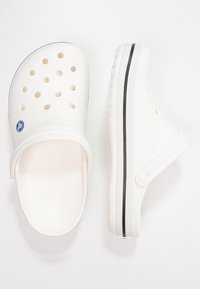 Hvite plastklogger med perforeringer for ventilasjon, en svart akcentstripe og en bakre stropp for et sikkert grep. Rund tådesign.
