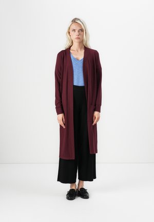 Cardigan long bourgogne sur un haut bleu à col en V, associé à un pantalon noir à jambes larges et des chaussures noires. Texture lisse, design à l'avant ouvert.