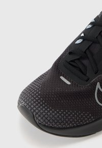 Schwarze Sneaker mit strukturiertem Mesh-Obermaterial, Gummisohle und reflektierenden Details. Verfügt über eine Schnürung und eine gepolsterte Zunge.