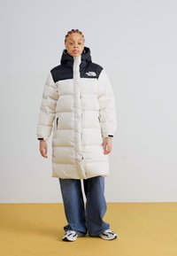 Witte puffer jas met een zwarte capuchon, voorzien van horizontale stiksels, ritssluiting, zijzakken en een logo-accent op de borst.