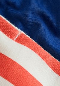 Gros plan d'un tissu doux avec des rayures horizontales rouges et blanches à côté d'un matériau tricoté bleu uni offrant des détails nets de texture.