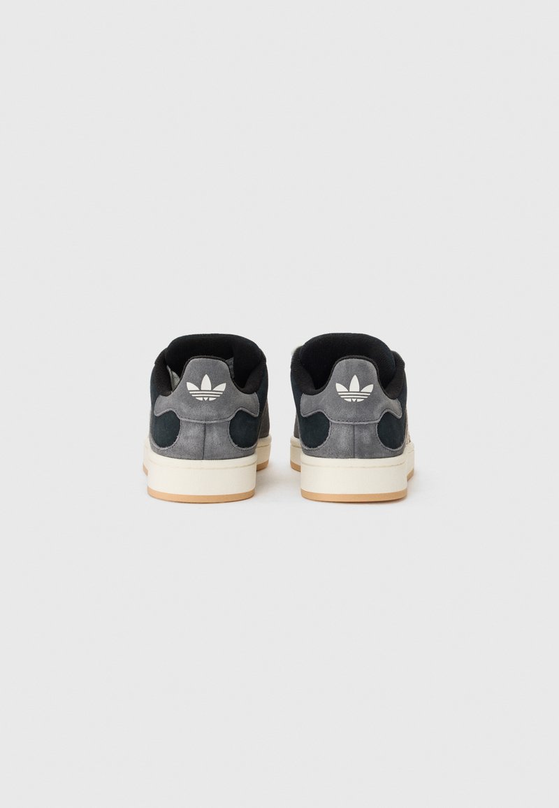 Zapatillas negras y grises con un logo blanco en el talón, sobre un fondo blanco liso. Los zapatos tienen un acabado texturizado.