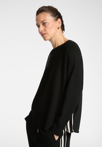 Suéter negro con un corte relajado, cuello acanalado y rayas verticales en contraste a los lados. Textura suave con un detalle sutil del logo.