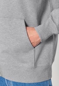 Felpa grigia con tasca frontale, polsini e orlo a coste. Il materiale sembra liscio ed elasticizzato, progettato per comfort e abbigliamento casual.