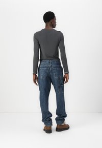 Γκρι μακρυμάνικη μπλούζα συνδυασμένη με φαρδιά μπλε τζιν παντελόνια. Τα τζιν διαθέτουν πολλές τσέπες και γυρισμένα τελειώματα, συμπληρωμένα με καφέ μπότες.