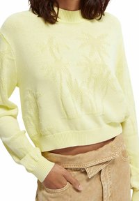 Suéter de punto amarillo con un diseño corto, cuello y puños acanalados, con patrones de palmeras sutilmente tejidos en la tela.