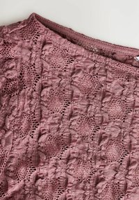 Roze kantweefsel met een bloemendessin en verfijnde details, met een gestructureerd oppervlak. Elasta gecentreerde rand voor extra rek.