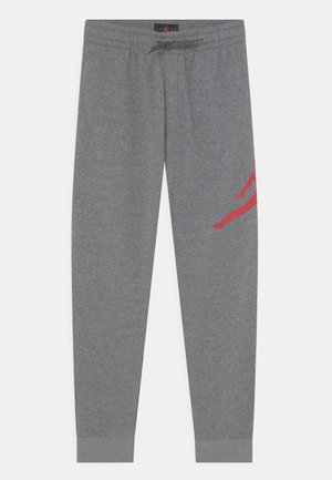 Pantalon de survêtement gris avec taille élastique et cordon, avec un graphique partiel de silhouette rouge sur la cuisse droite.