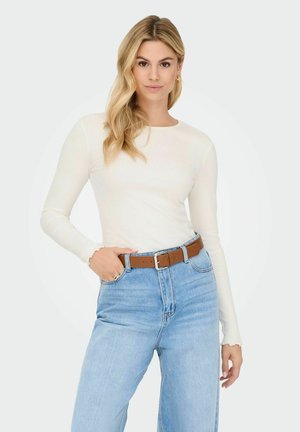 Long-sleeve, ribbed white top paired with high-waisted light blue jeans; brown leather belt with silver buckle; smooth texture and fitted design.