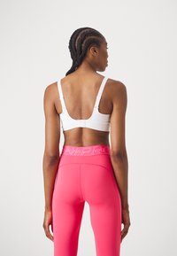 Hvit sports-bh med justerbare stropper og hakefeste bak, kombinert med høyt liv, lyserosa leggings med logo-bånd.