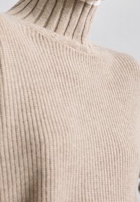 Närbild av en beige stickad polotröja som visar en ribbad krage och textilstruktur på övre delen av kroppen.