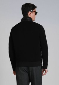 Zwarte ribgebreide trui met een elegante, glanzende zwarte kraag. Heeft lange mouwen en een aangesloten tailleband, weergegeven vanaf de achterkant.