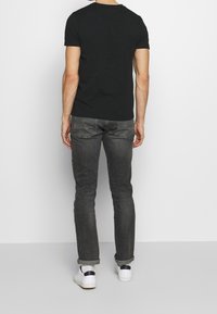 Camiseta de algodón negra con un clásico escote redondo, combinada con unos jeans ceñidos gris oscuro. Zapatillas blancas con detalles en azul marino completan el conjunto.