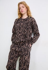 Pulover z leopardjim vzorcem v rjavi in črni barvi, dolgi rokavi in okroglo ovratnik, narejen iz mehkega, teksturiranega materiala. Vidne so tudi usklajene hlače.