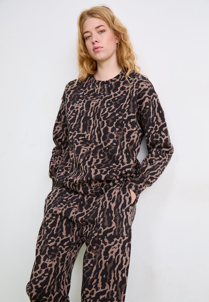 Brun og sort leopardmønstret sweatshirt med langeærmer og rund halsudskæring, lavet af blødt, struktureret stof. Matchende bukser synlige.